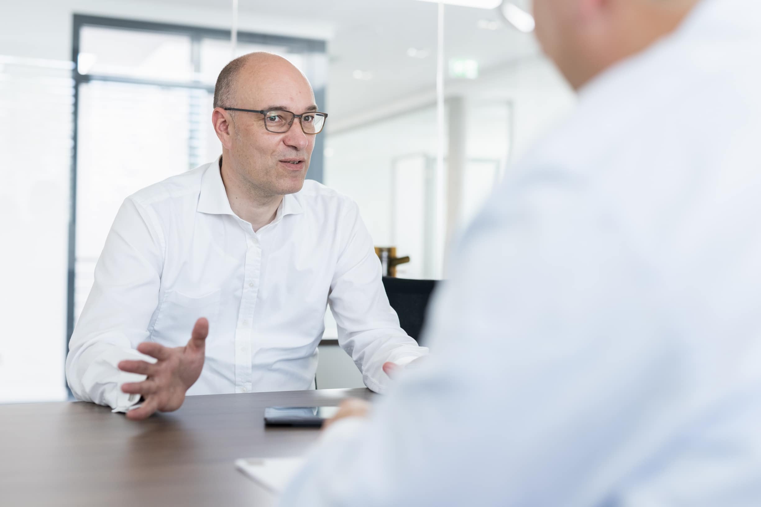 Zwei Gesprächspartner im Besprechungsraum, einer erläutert mit den Händen einen Sachverhalt